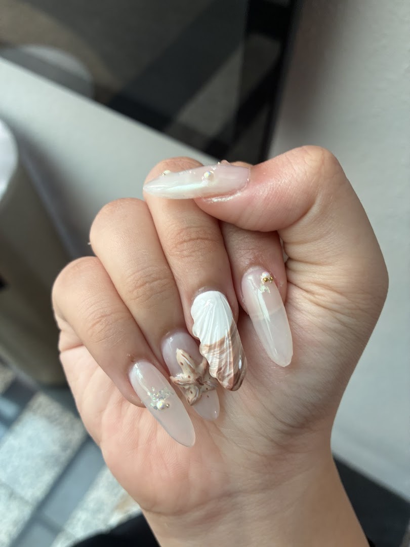 A hand showcasing elegant long nails with intricate seashell and starfish 3D designs.