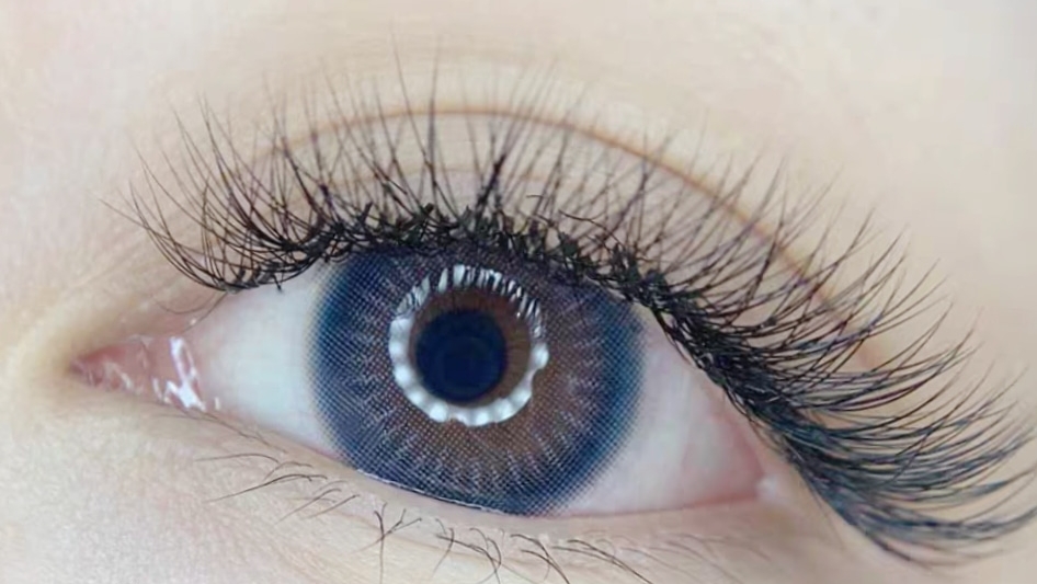 Close-up of an eye showcasing voluminous lash extensions and a colored contact lens.
