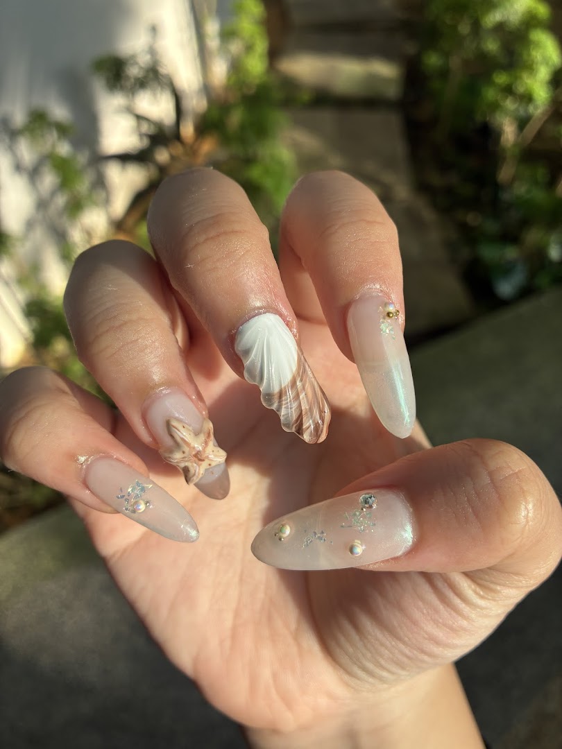 Close-up of a hand showcasing long, intricately designed nails with seashell and starfish embellishments.