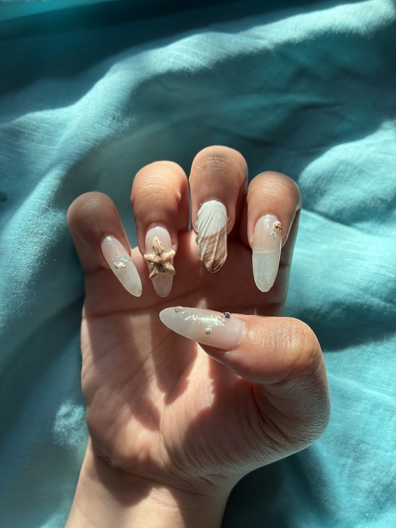 Close-up of a hand showcasing intricate nail art with seashell and starfish designs.