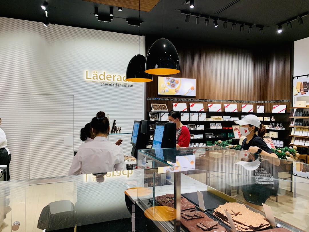 Interior view of Läderach chocolate shop with staff, display counter, and branded products.