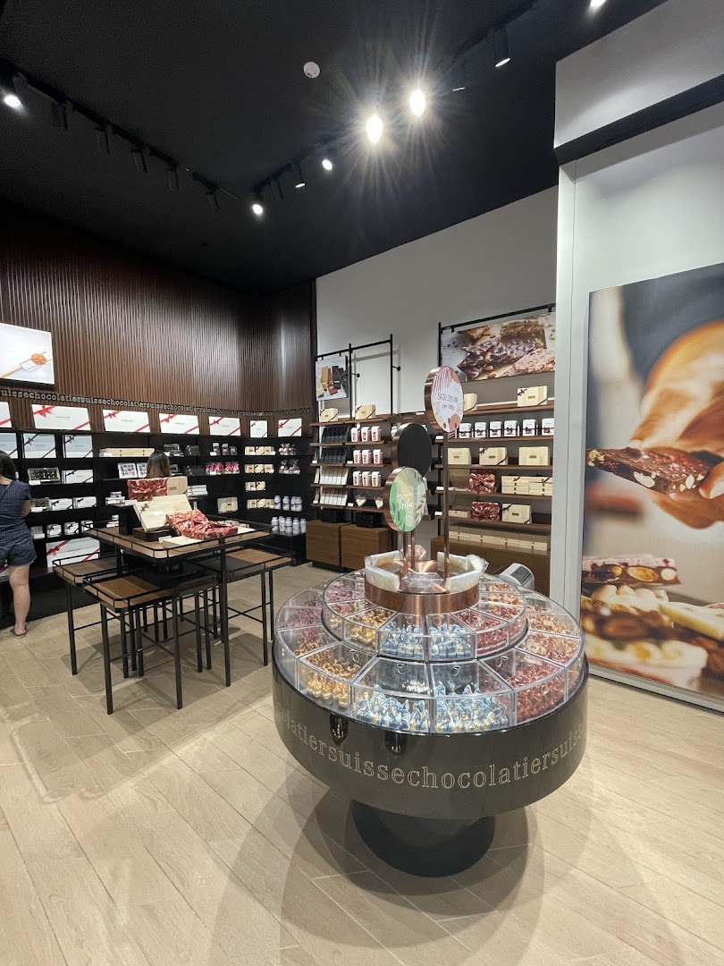 Interior view of a Läderach chocolate shop, featuring diverse chocolate displays and a customer browsing.