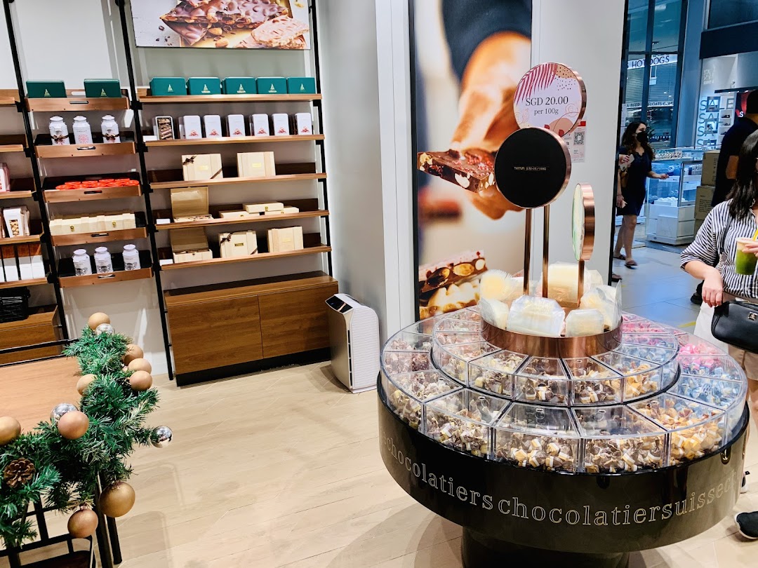 An inviting interior view of Läderach chocolate shop, featuring a large fresh chocolate display and product shelves.