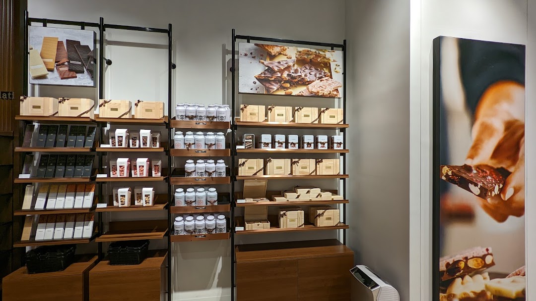 Interior view of a chocolate shop displaying various premium chocolate bars, gift boxes, and confections on shelves.