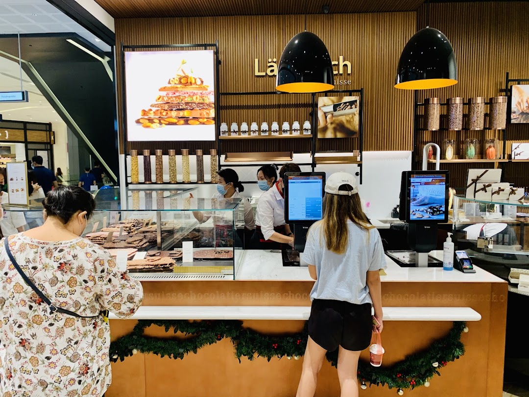 Customers browse and purchase exquisite chocolates at the Läderach counter, showcasing a vibrant retail experience.