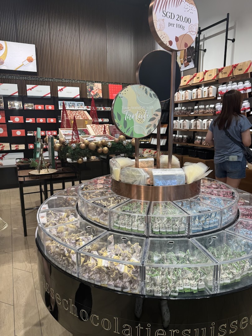 Interior view of a Läderach chocolate shop featuring a large circular display of assorted chocolates.