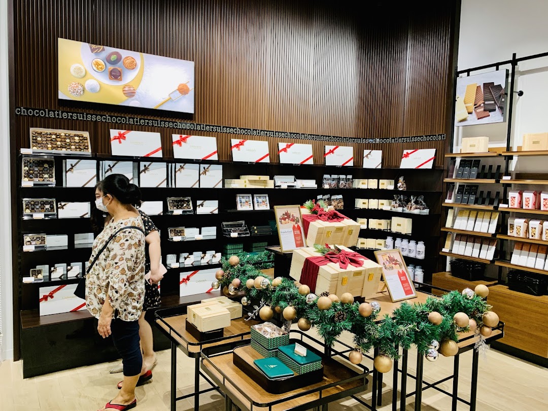 Interior view of a Läderach chocolate shop with customers browsing various chocolate products and gift boxes.
