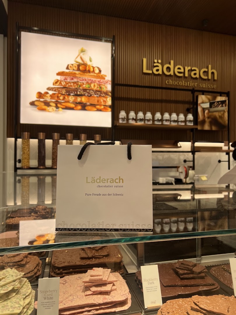 A vibrant display of artisanal chocolates and a branded shopping bag inside a Läderach store.