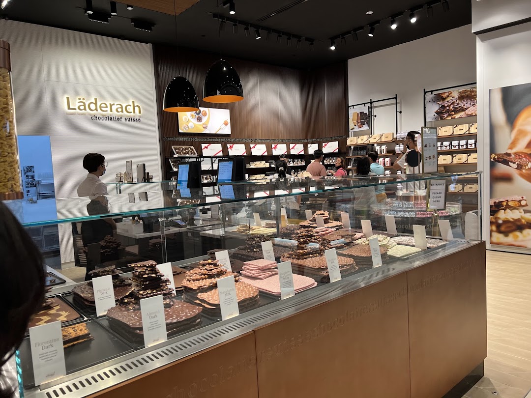 Interior view of a Läderach chocolate shop with a large display of fresh chocolate slabs and customers.