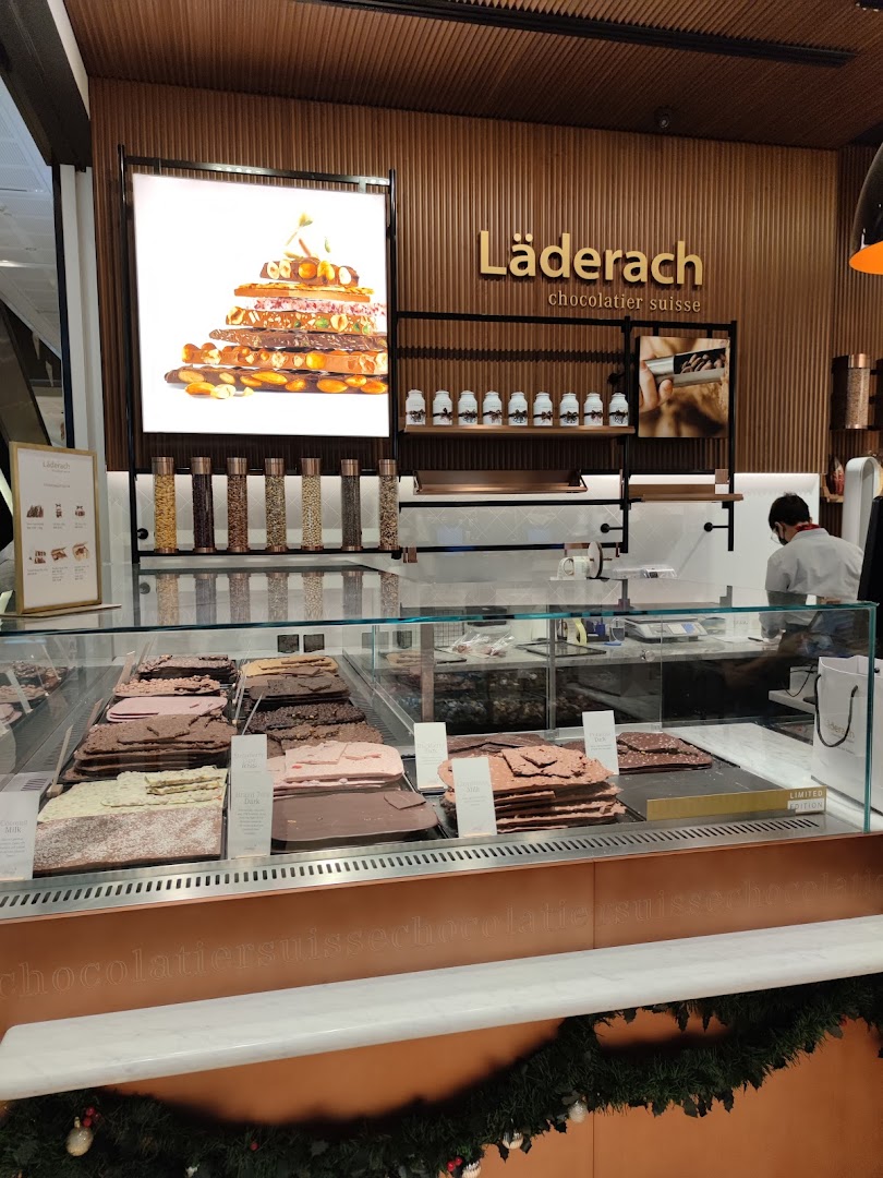 Interior view of Läderach chocolate shop, showcasing fresh chocolate slabs and a staff member.