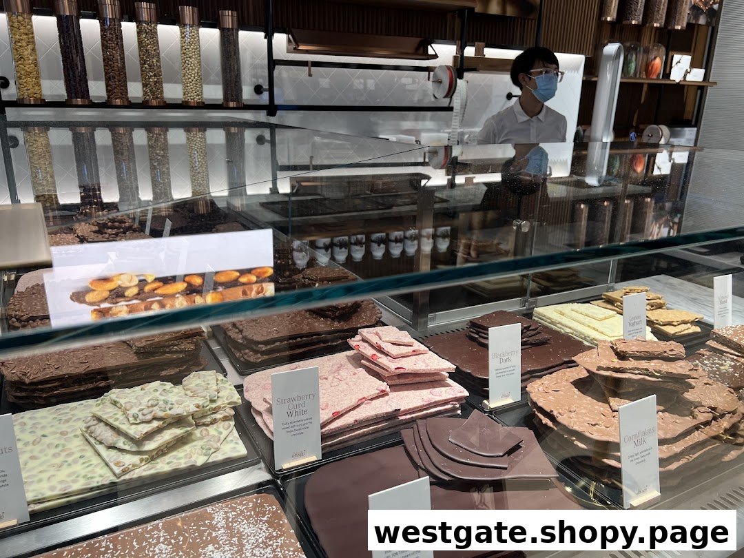 A vibrant display of fresh chocolate slabs and pralines in a glass case at Läderach, with a staff member visible.