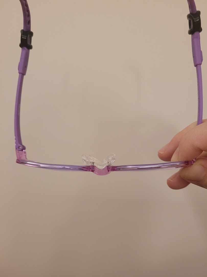 A close-up of purple eyeglasses with a clear nose bridge, held by a hand.
