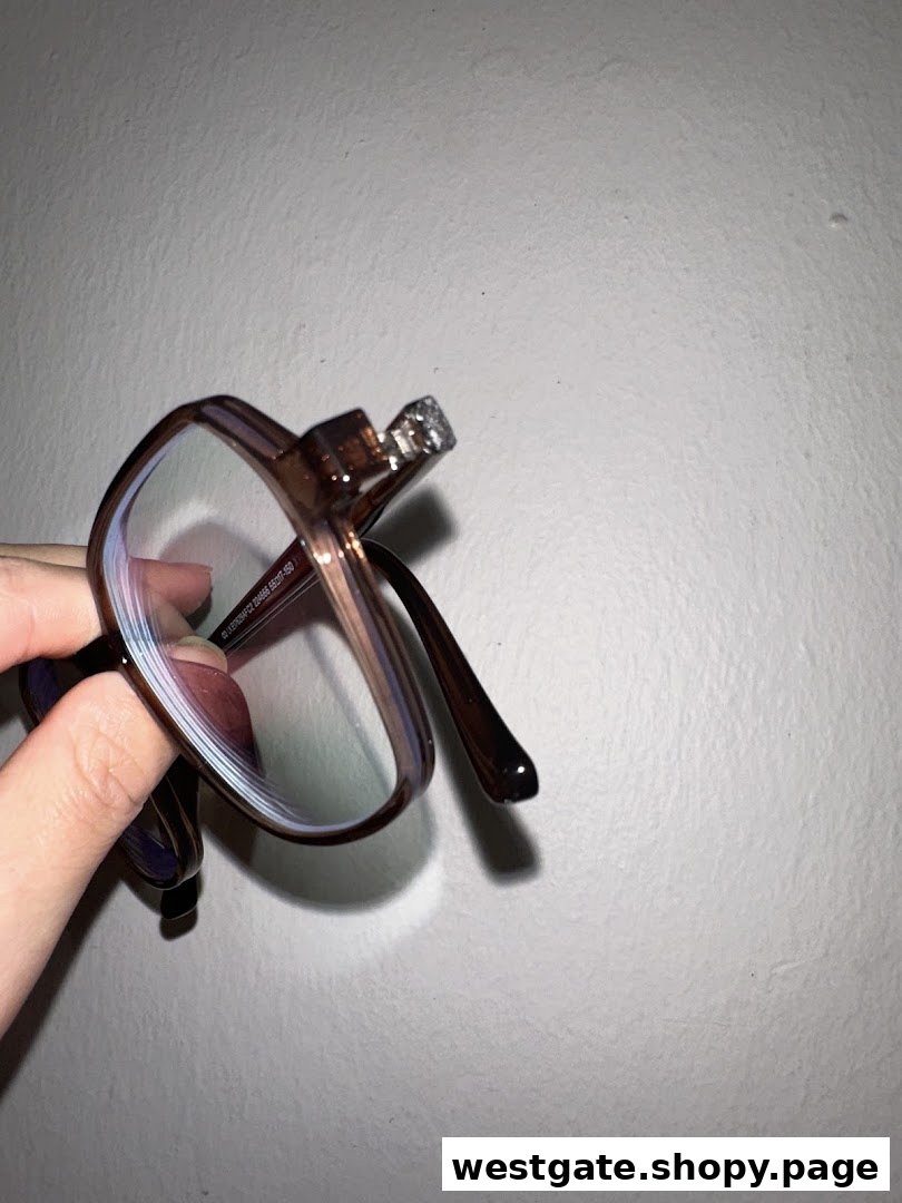 A hand holds a pair of stylish brown eyeglasses with clear lenses against a white wall.