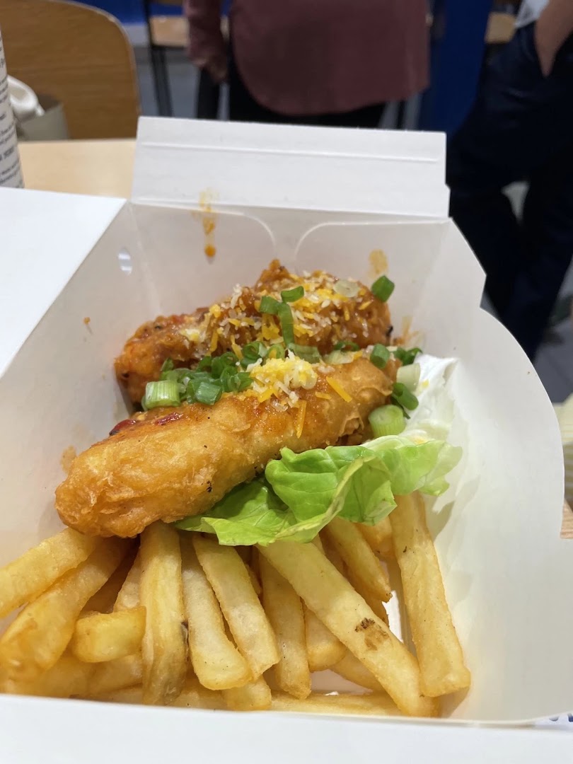 A takeout box filled with golden-fried fish, crispy fries, fresh lettuce, and savory toppings.