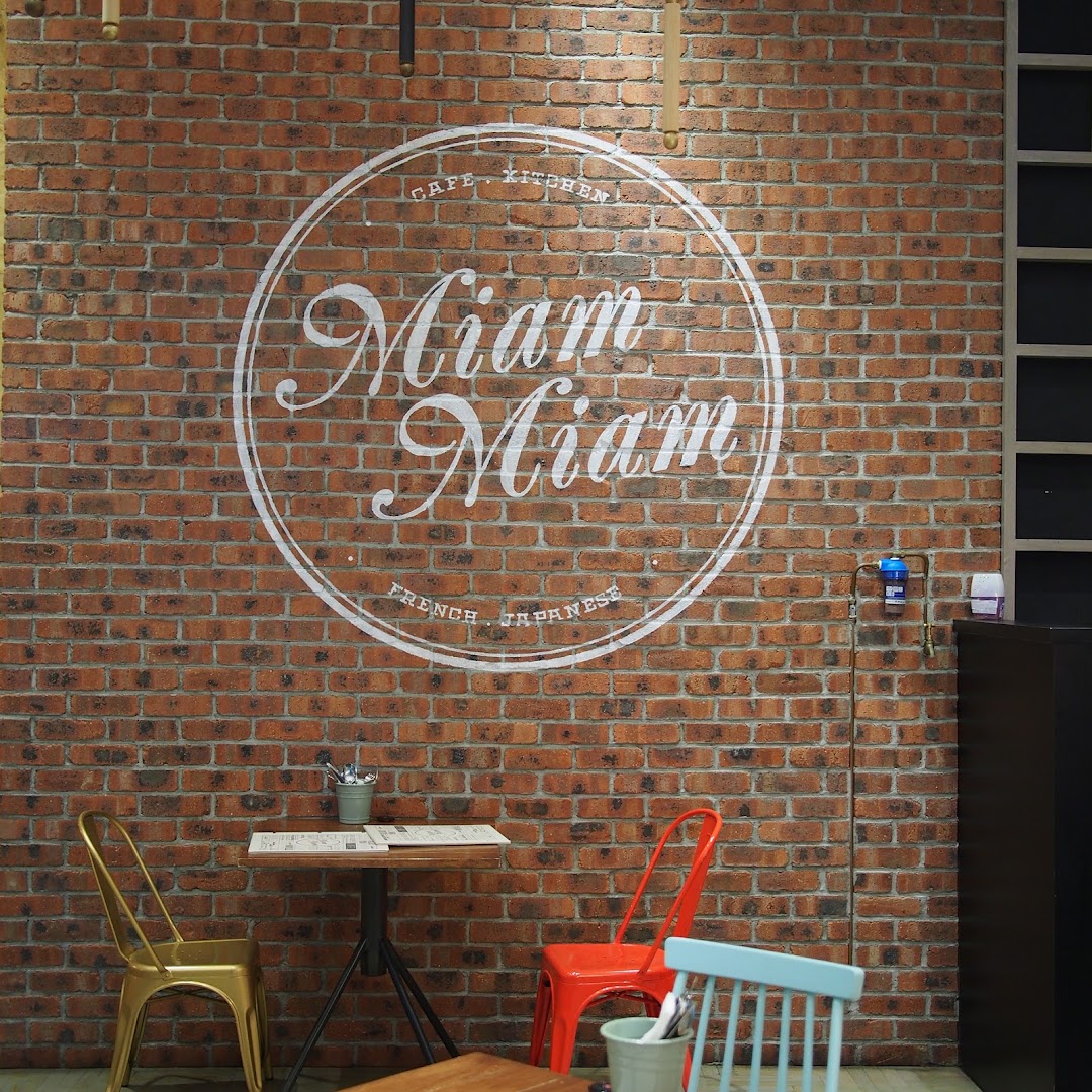 Interior view of Miam Miam cafe featuring a brick wall with its French-Japanese logo and seating.