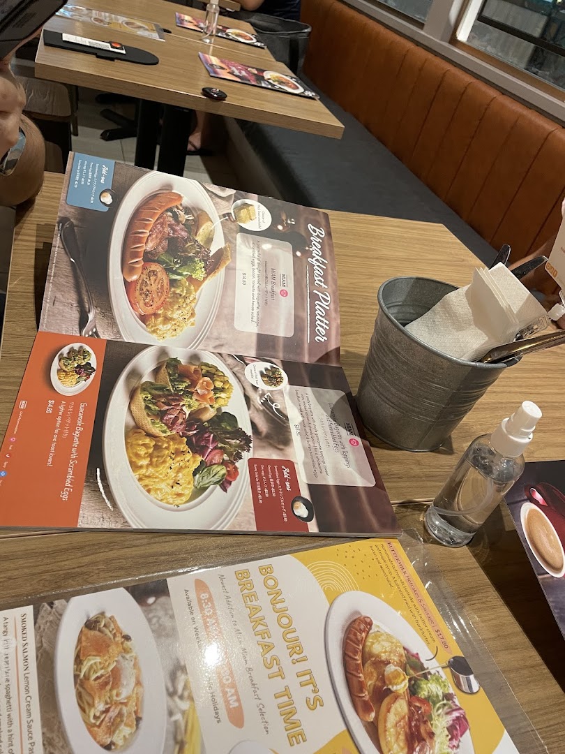 A detailed menu displaying various breakfast and pasta dishes on a wooden table inside a cafe.