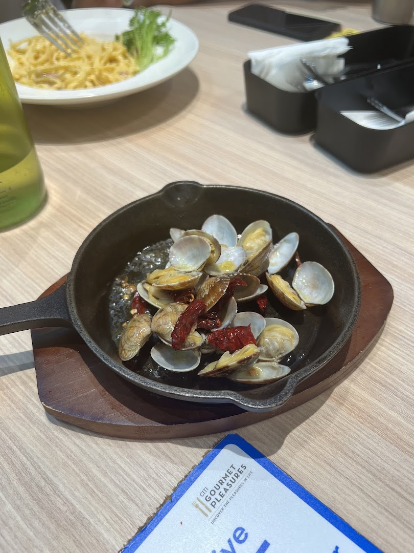 A close-up of a sizzling clam dish and pasta on a wooden table in a restaurant setting.