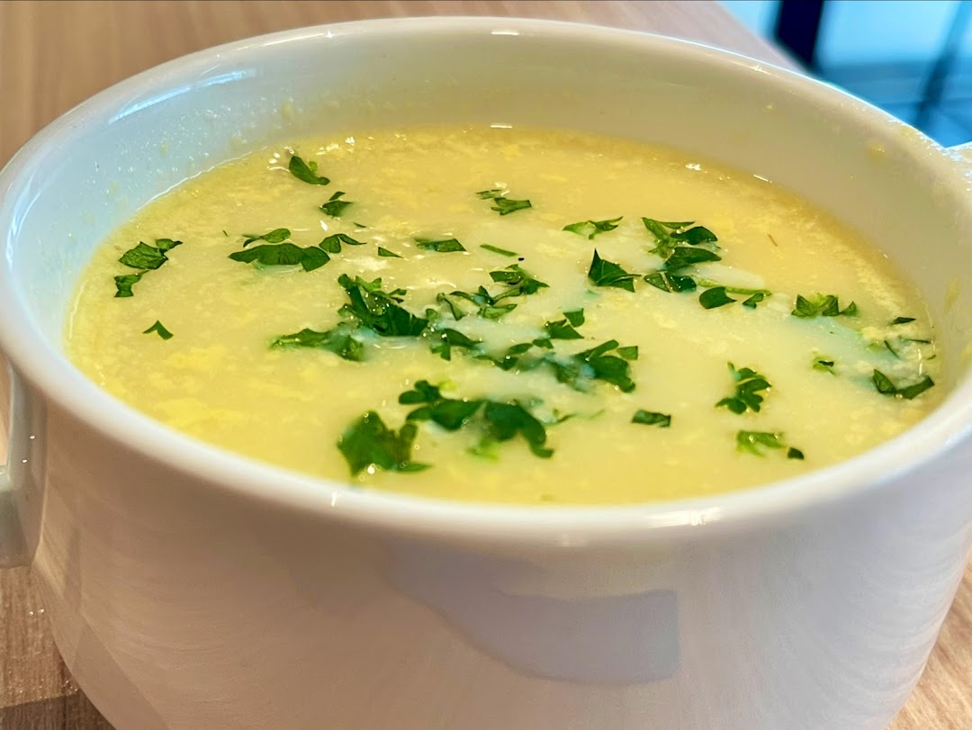 A close-up of a creamy yellow soup garnished with fresh green herbs in a white mug.