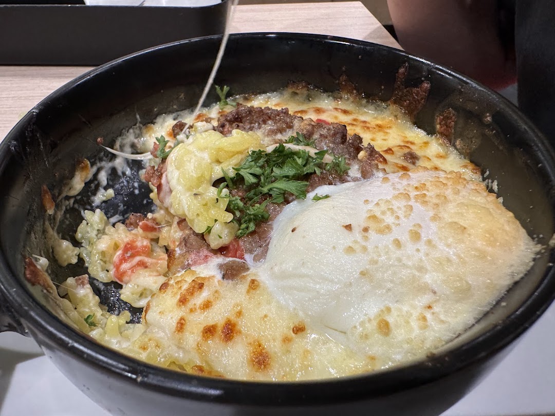 A close-up of a bubbling, cheesy baked dish with ground meat, pasta, and herbs.