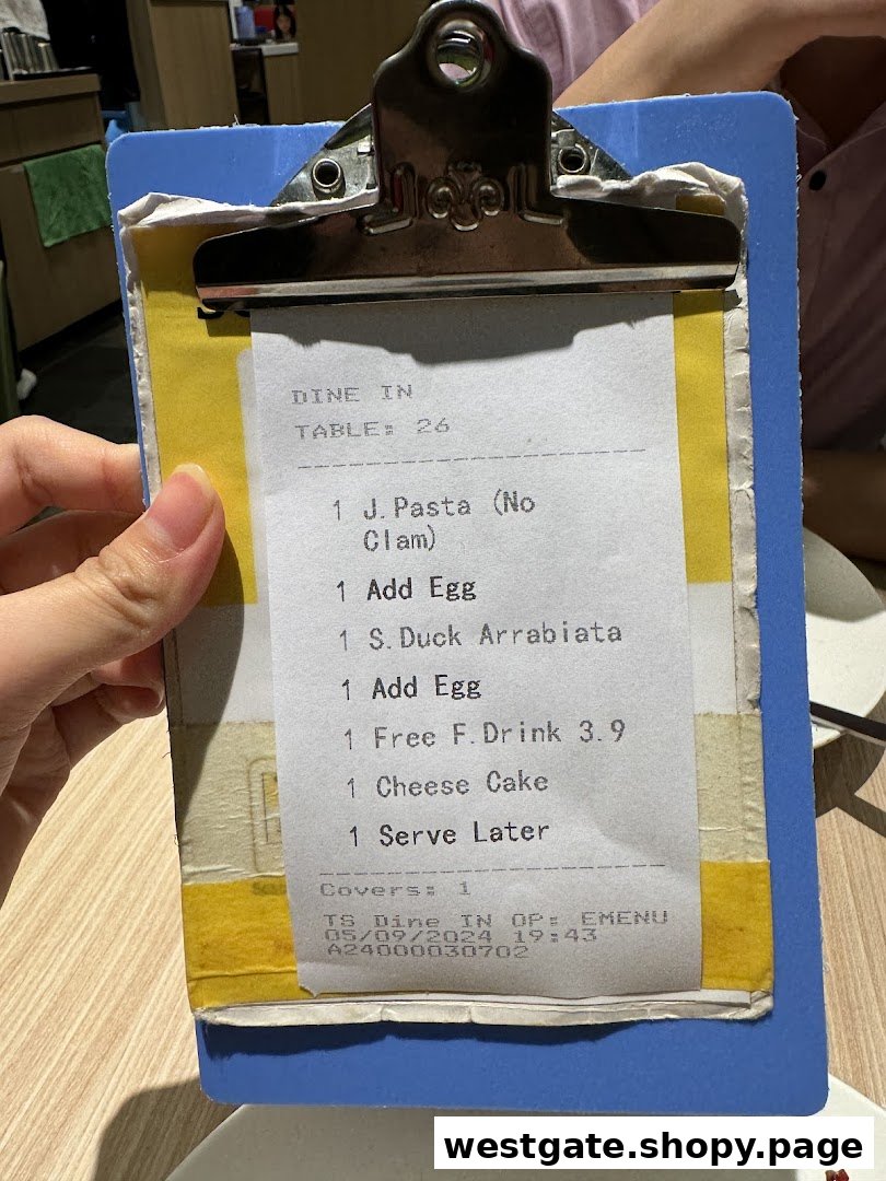 A hand holds a clipboard displaying a dining order slip from Milan Shokudo with various food and drink items.