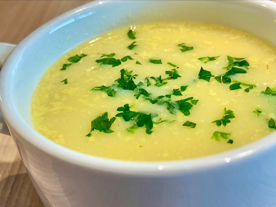 A close-up of a creamy yellow soup garnished with fresh green parsley in a white bowl.