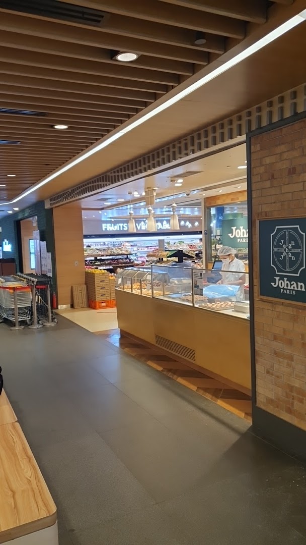 View of the Johan Paris bakery counter at the entrance of a supermarket, with fresh produce visible inside.