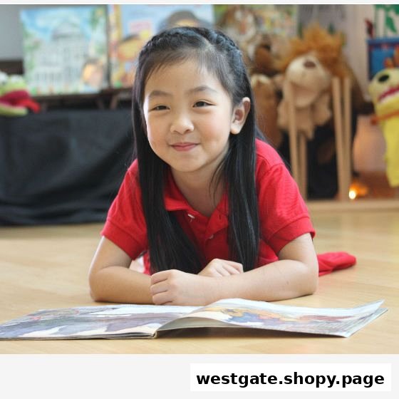 A young girl in a red shirt smiles while reading a book on the floor.