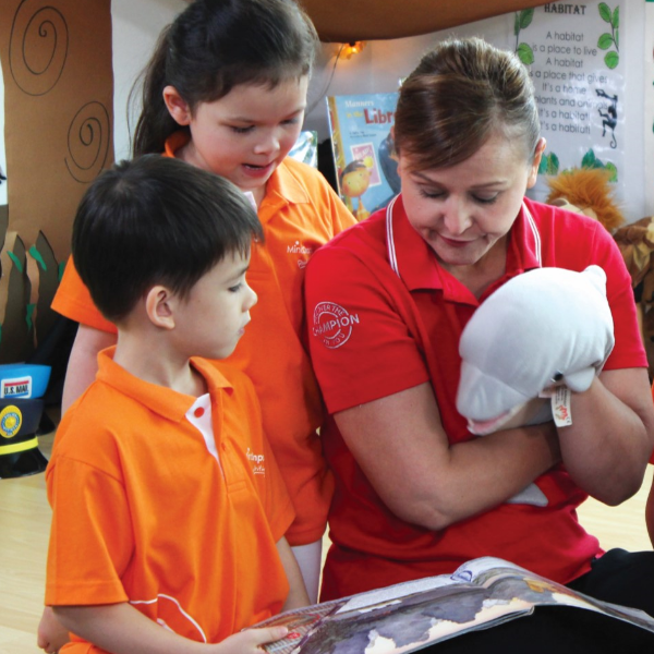 An adult reads to two children in an engaging learning environment at MindChamps.