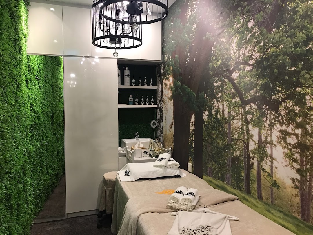A serene aesthetic treatment room featuring a comfortable bed, green wall, and a calming forest mural.