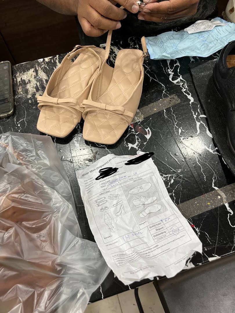 A pair of beige shoes on a counter with a service form and hands working on an item.