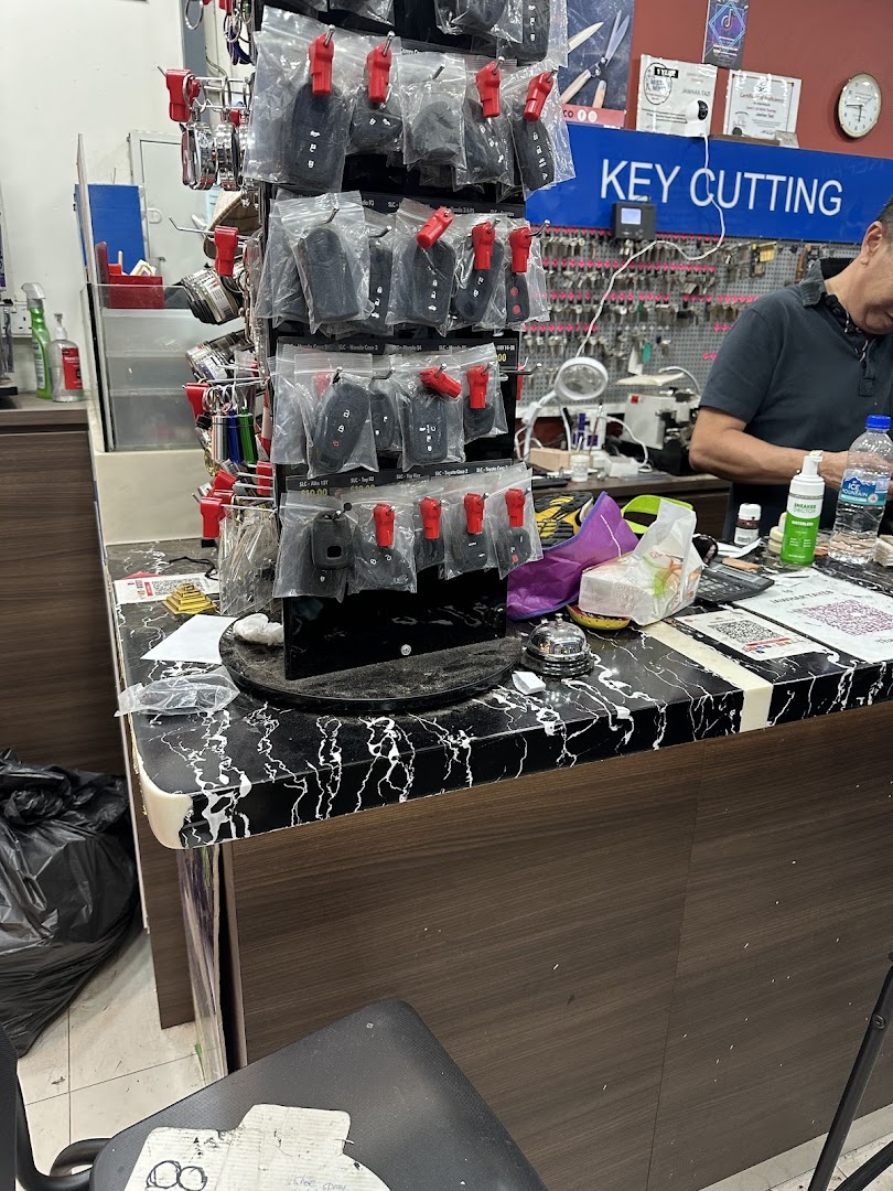 Interior view of Mister Minit counter, showing key fobs, a 'KEY CUTTING' sign, and a staff member.