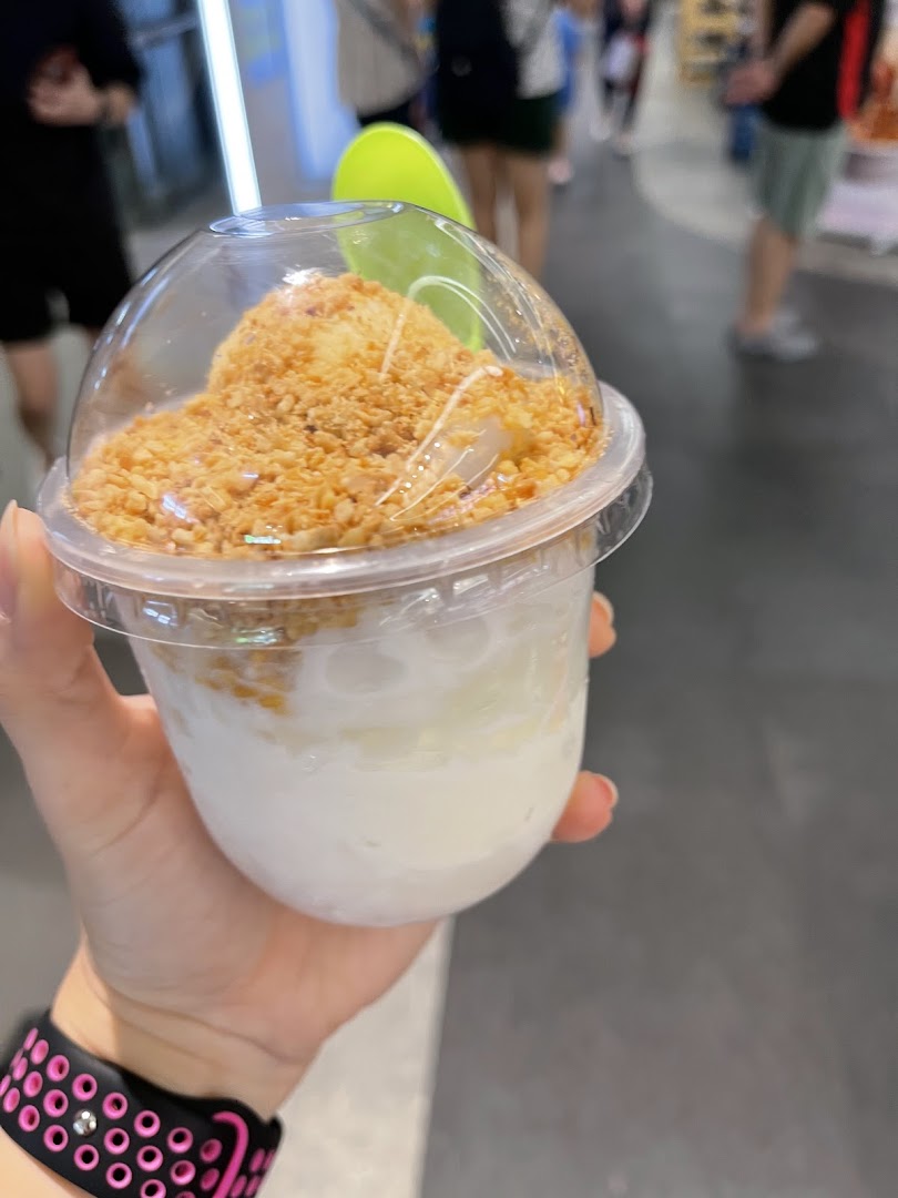 A hand holds a clear cup filled with a coconut dessert topped with crushed peanuts.