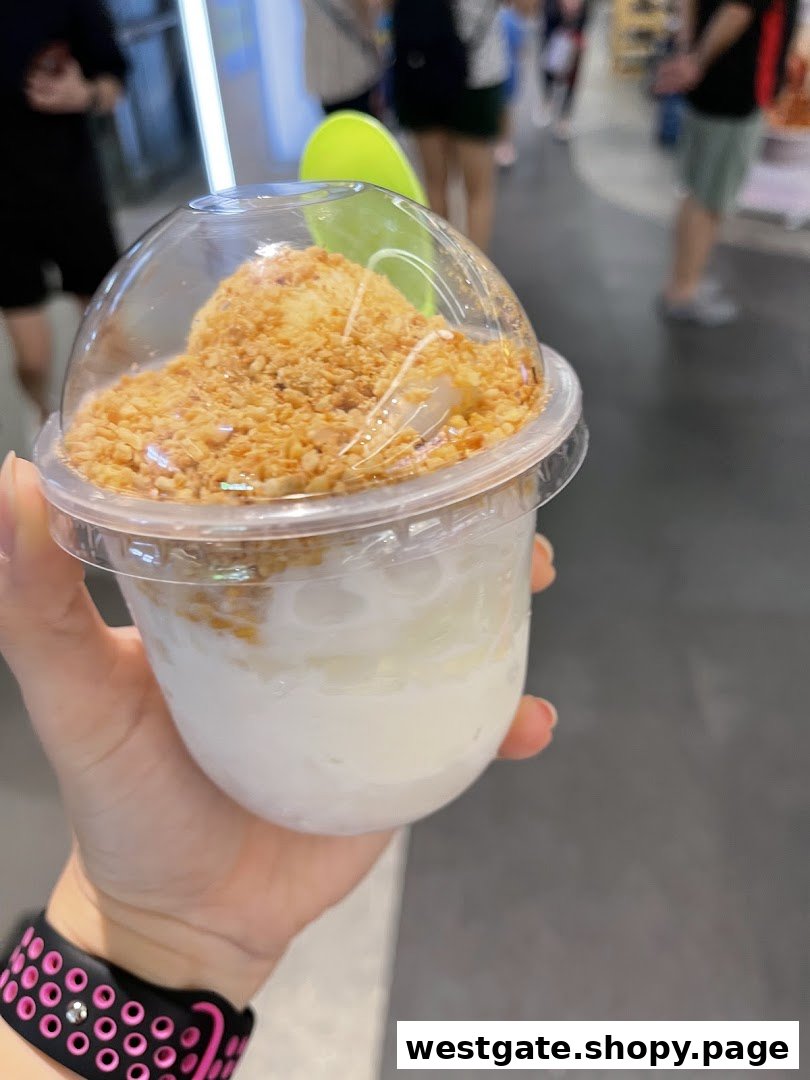 A hand holds a clear cup filled with a coconut dessert topped with crushed peanuts.