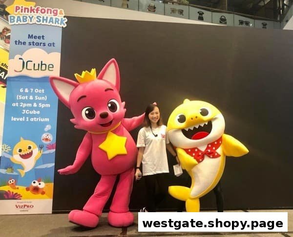 A woman poses with Pinkfong and Baby Shark mascots next to an event banner at JCube.