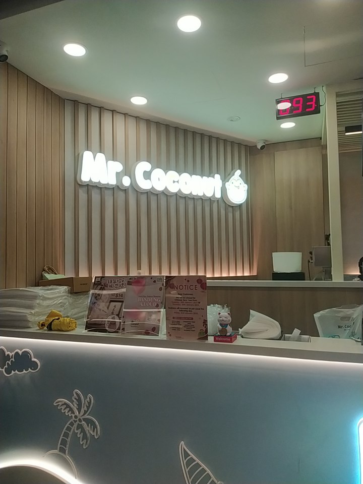 Interior view of the Mr. Coconut shop counter with its illuminated logo and a digital queue number display.