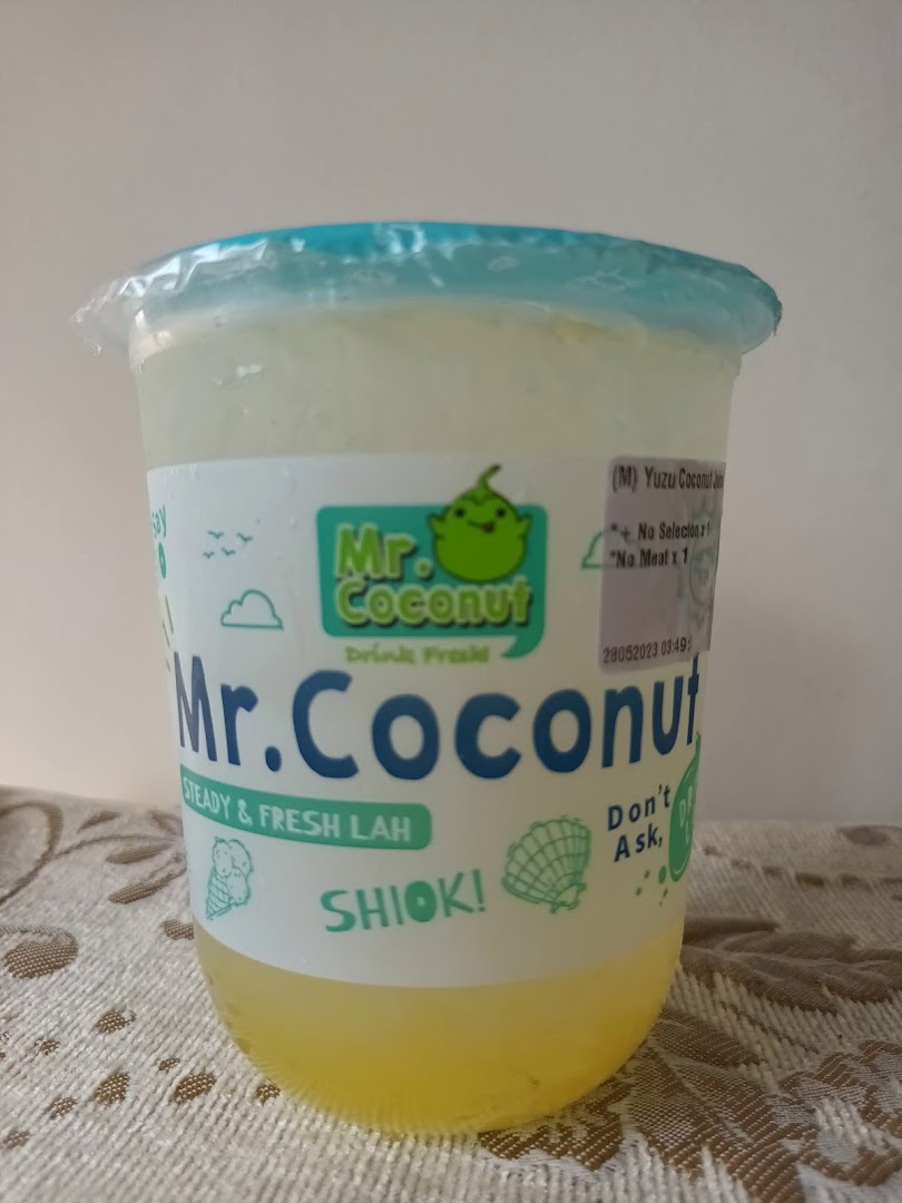 A clear plastic cup of Yuzu Coconut drink from Mr. Coconut, featuring the brand's logo and slogans.