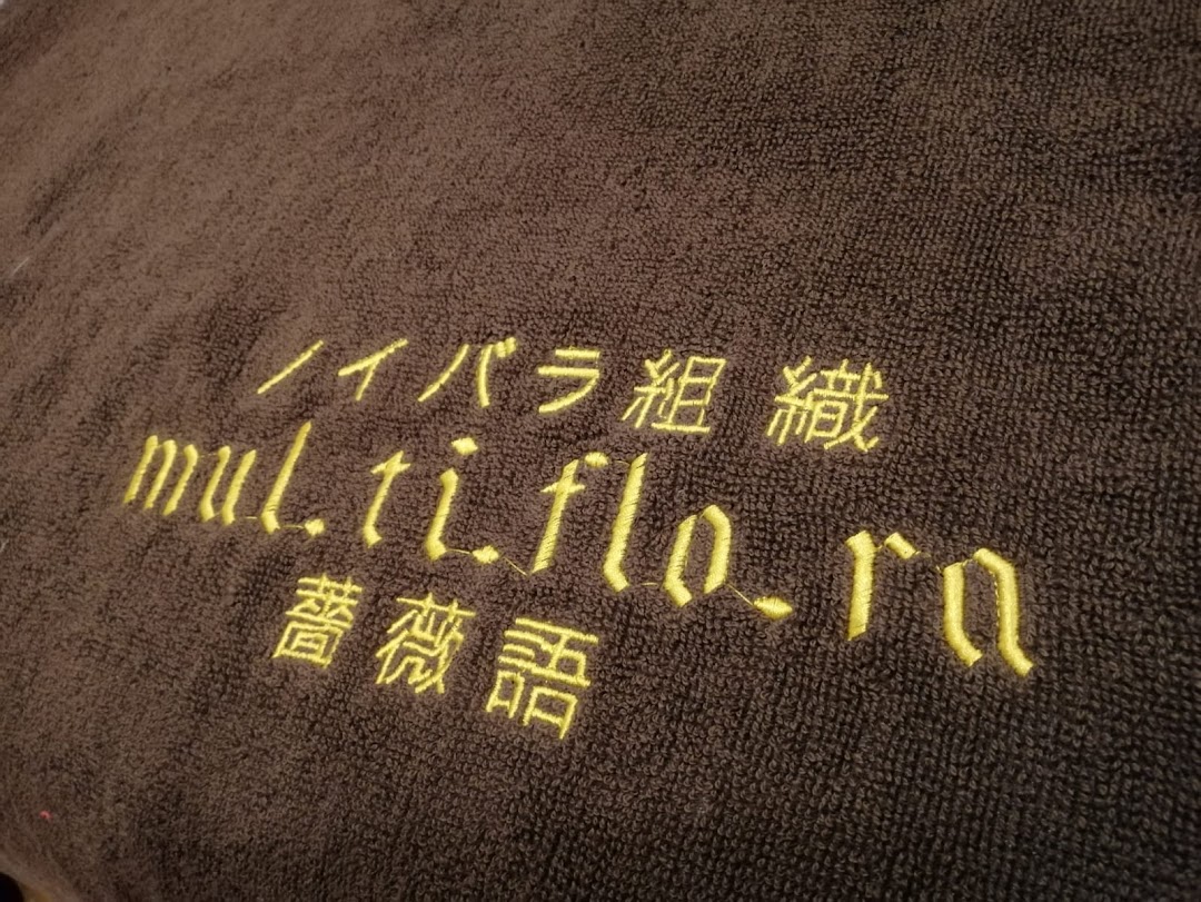 Close-up of a brown towel with 'multiflora' and Japanese text embroidered in yellow.