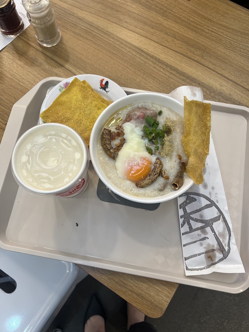 A hearty bowl of congee with an egg, meat, fried dough, and a drink on a tray.