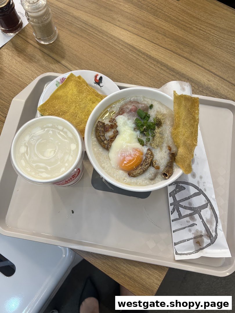 A hearty bowl of congee with an egg, meat, fried dough, and a drink on a tray.