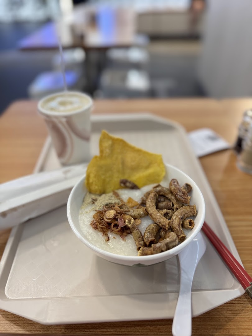 A bowl of congee with crispy toppings, a fried pastry, and a drink on a tray.