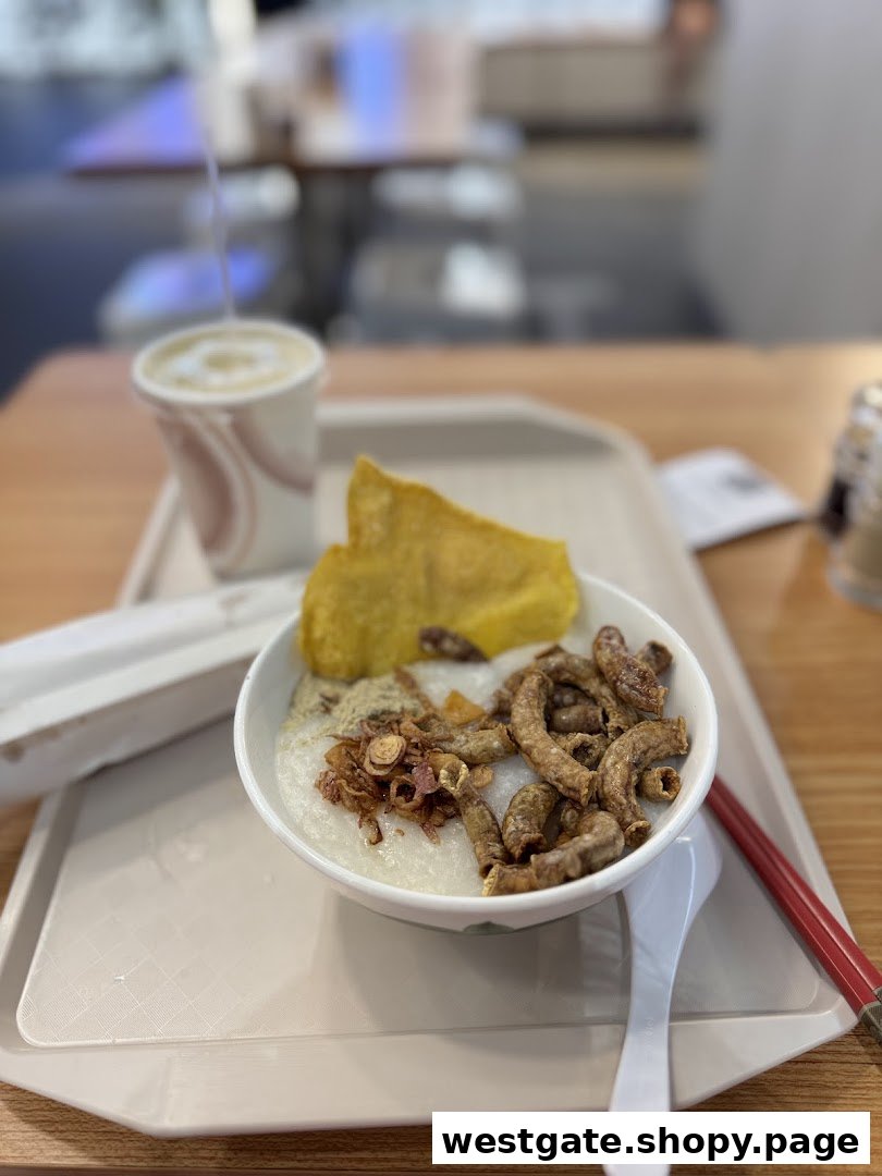 A bowl of congee with crispy toppings, a fried pastry, and a drink on a tray.