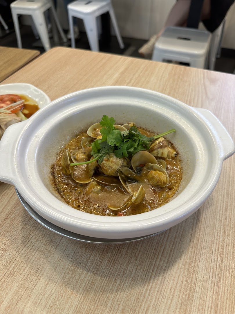 A ceramic pot filled with savory clams and broth, garnished with fresh cilantro, on a wooden table.