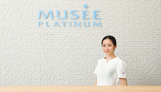 A friendly staff member stands in front of the Musee Platinum Tokyo branding wall.