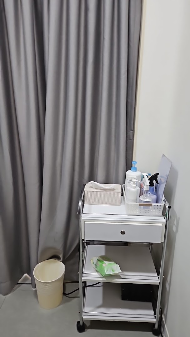 A utility cart with beauty products and supplies next to a grey curtain in a treatment room.