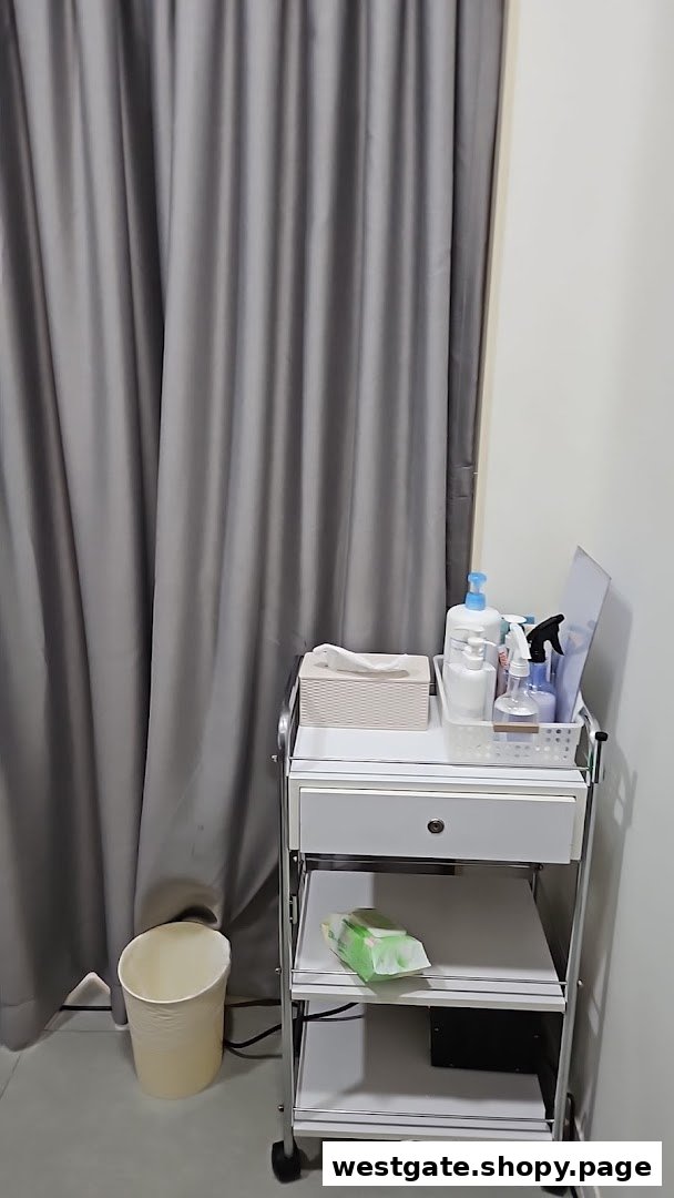 A utility cart with beauty products and supplies next to a grey curtain in a treatment room.