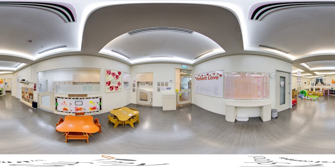 A bright, clean interior of a childcare center with small tables, chairs, and dedicated play areas.