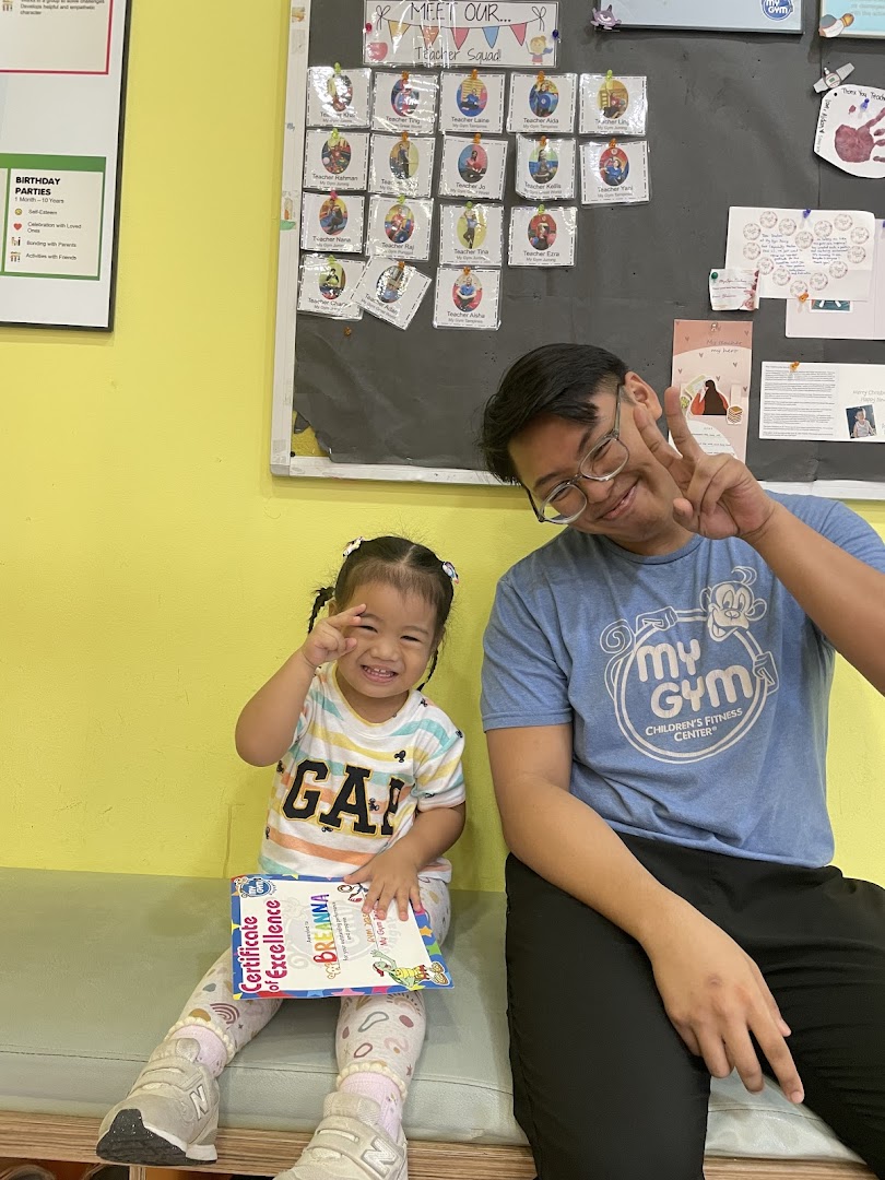 A happy child holding a certificate with a smiling adult in a My Gym Children's Fitness Center.