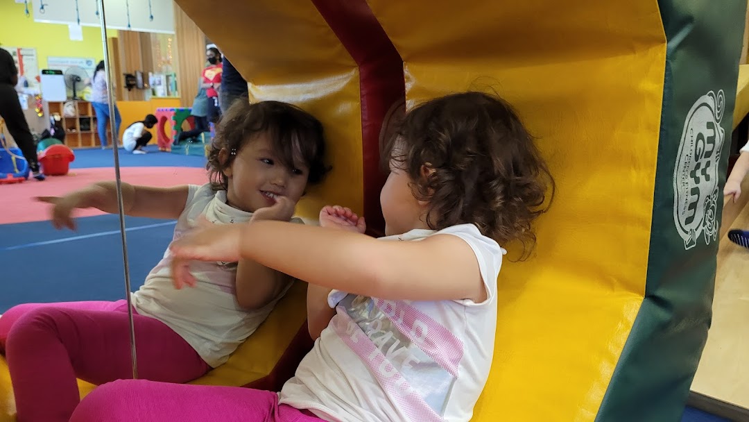 A young child smiles while interacting with a mirror in a vibrant children's fitness center.