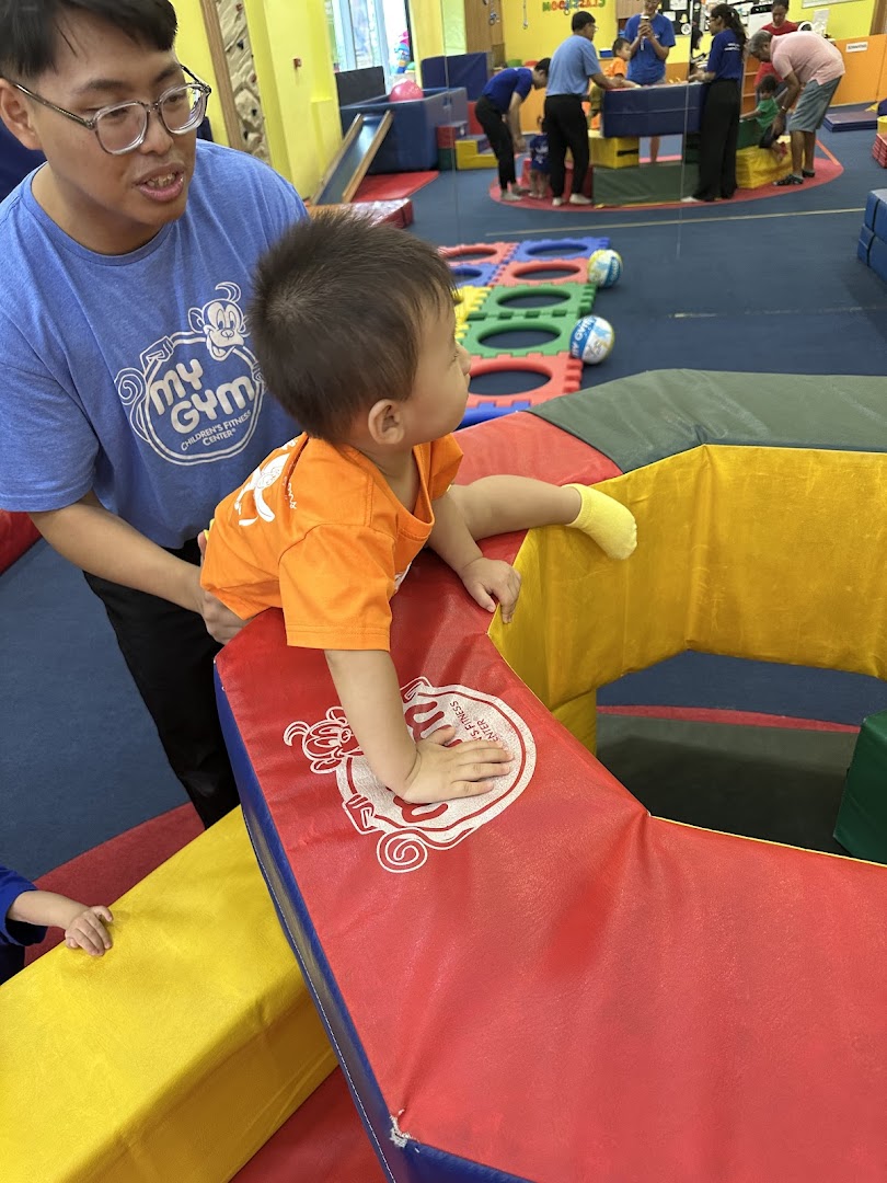 An instructor assists a young child on colorful soft play equipment at My Gym Children's Fitness Center.