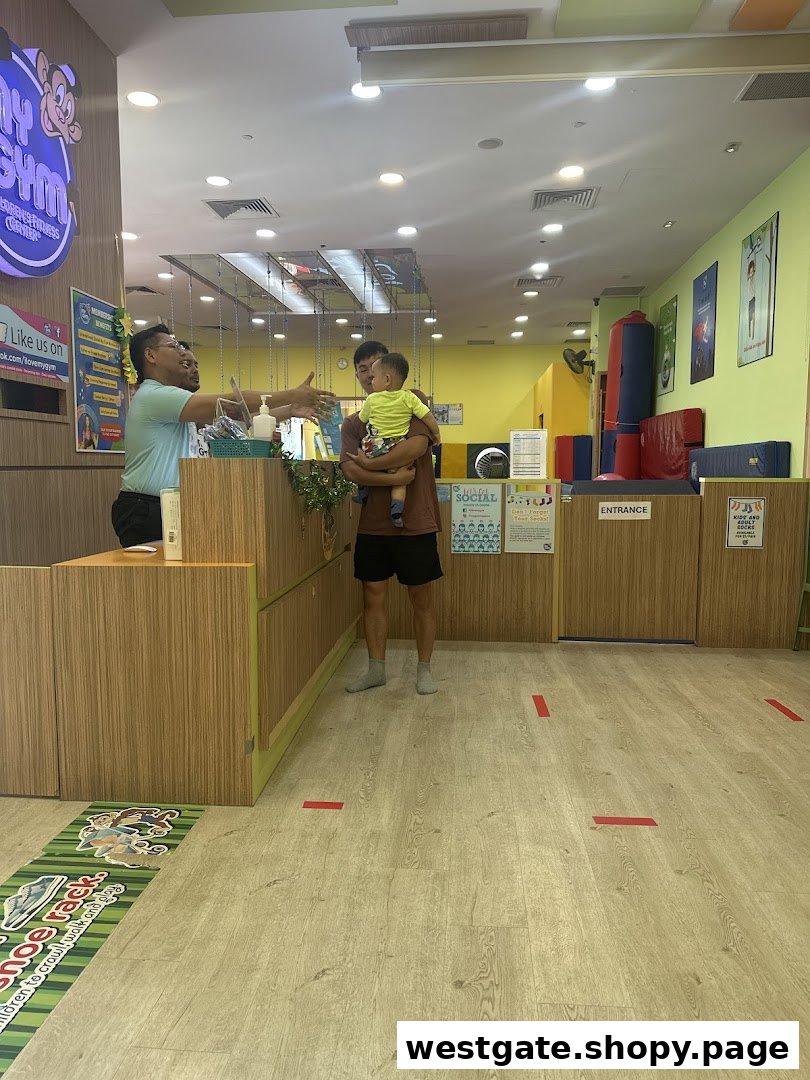 A staff member greets a parent and child at the reception of My Gym, with play areas visible.